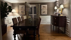 A dining room with a dark wooden table, six chairs, a chandelier, and framed bird artwork on the walls.
