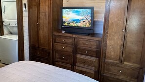 A bedroom with a bed, wooden cabinets, a washing machine, and a television on a wooden shelf.
