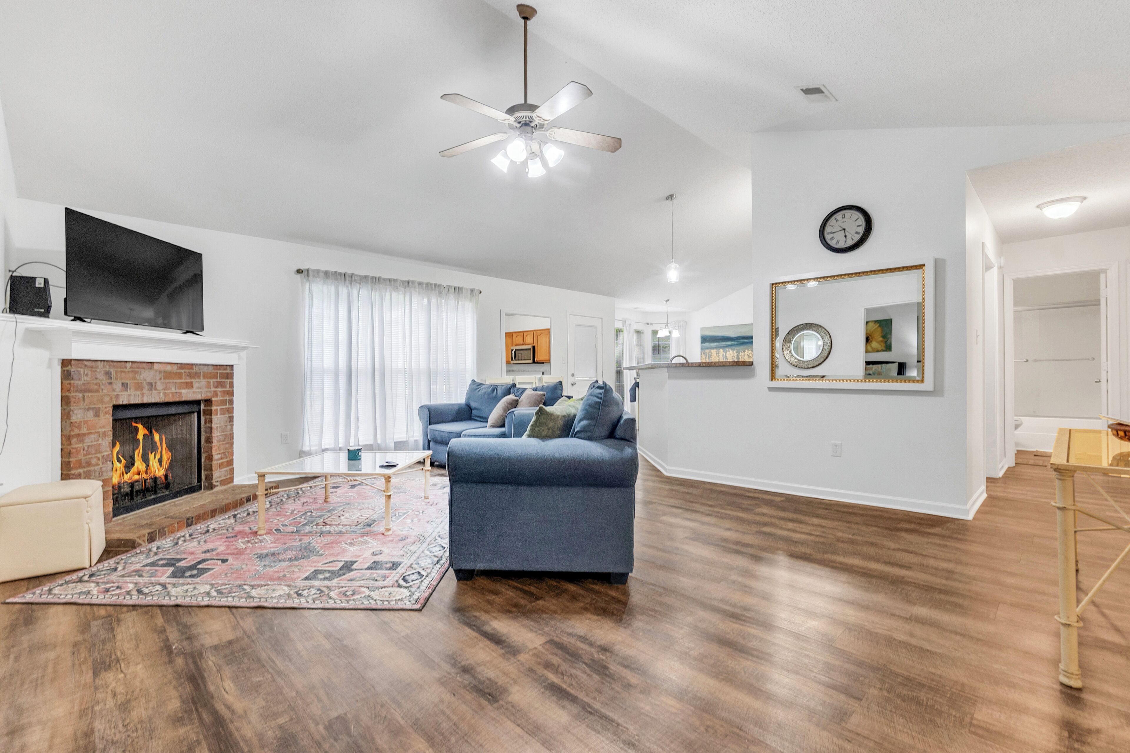 Un salon moderne avec une cheminée, un canapé bleu, un plancher en bois et un ventilateur de plafond.