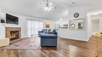 Un salon moderne avec une cheminée, un canapé bleu, un plancher en bois et un ventilateur de plafond.