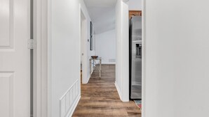 A narrow hallway with white walls and wooden flooring, leading to a kitchen area with a stainless steel refrigerator. - Warm & Charming 4-BR in the Heart of Southaven-Near Stateline, Silo Square. (Southaven)