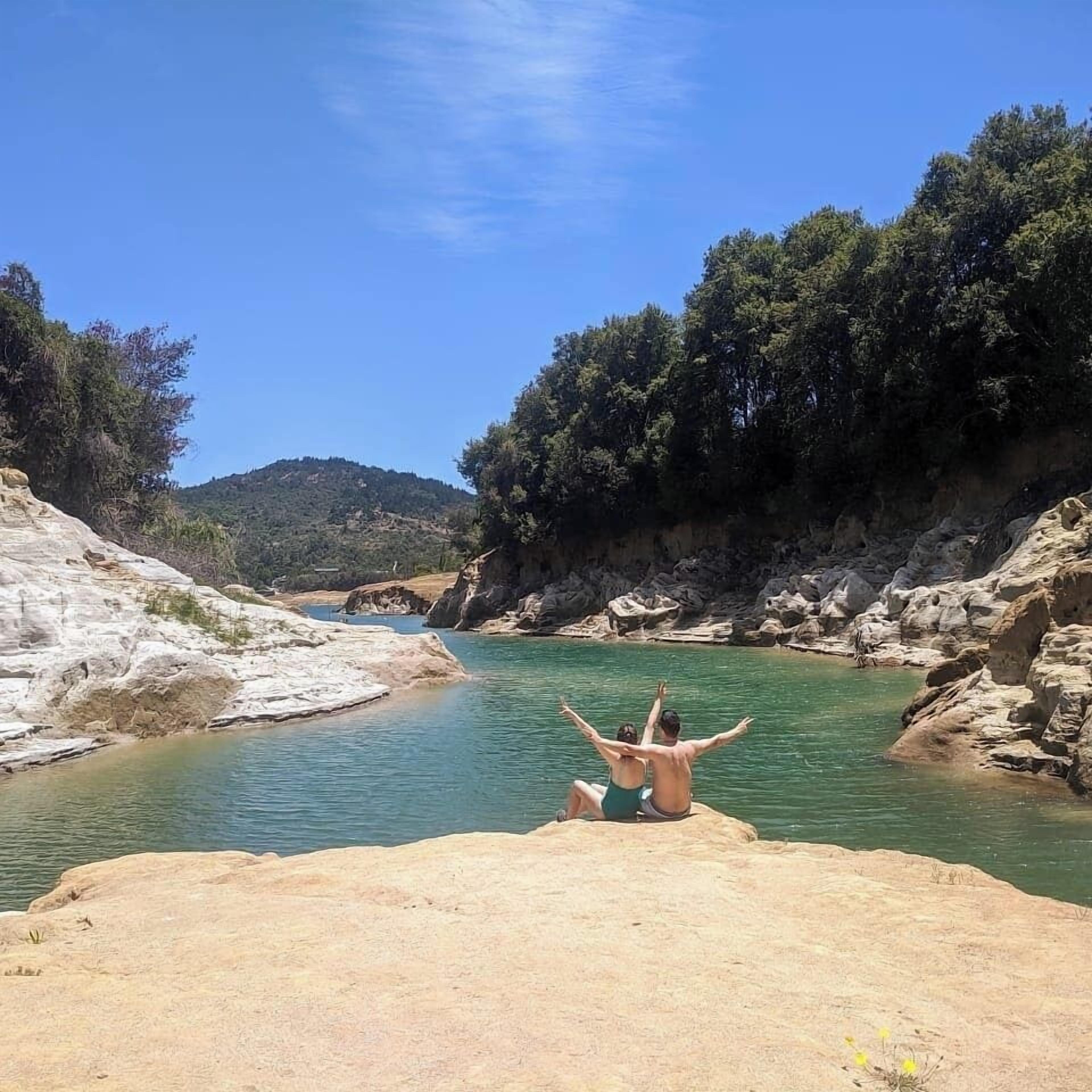 A rocky riverbank with a person sitting on a rock facing the water.