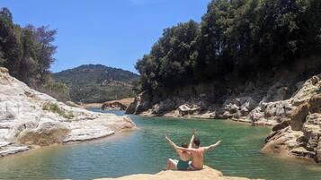 A rocky riverbank with a person sitting on a rock facing the water.