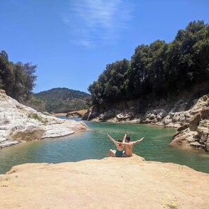 A rocky riverbank with a person sitting on a rock facing the water.