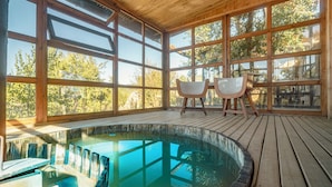 Une terrasse en bois avec un jacuzzi, de grandes fenêtres et deux chaises.