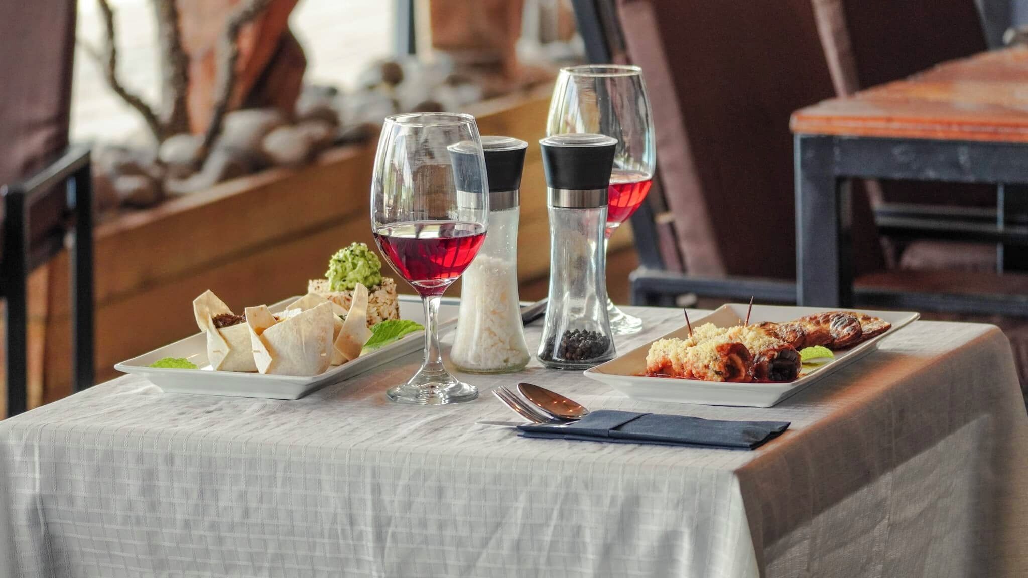 A table set with a plate of appetizers, two glasses of red wine, and a bottle of water.