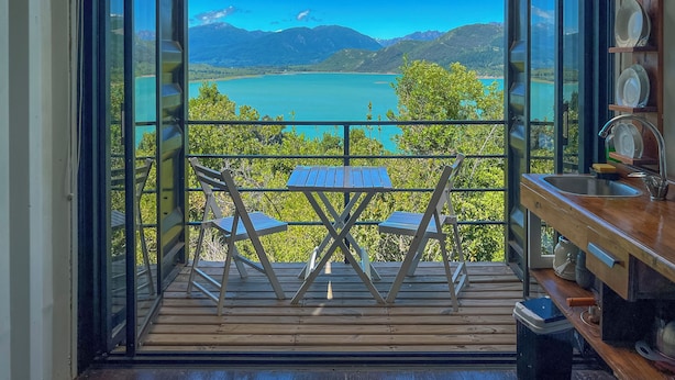 Un balcon avec une table et des chaises, donnant sur un lac et des montagnes.