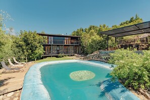 Una casa moderna con piscina, sillas de deck y un espacio exterior cubierto.