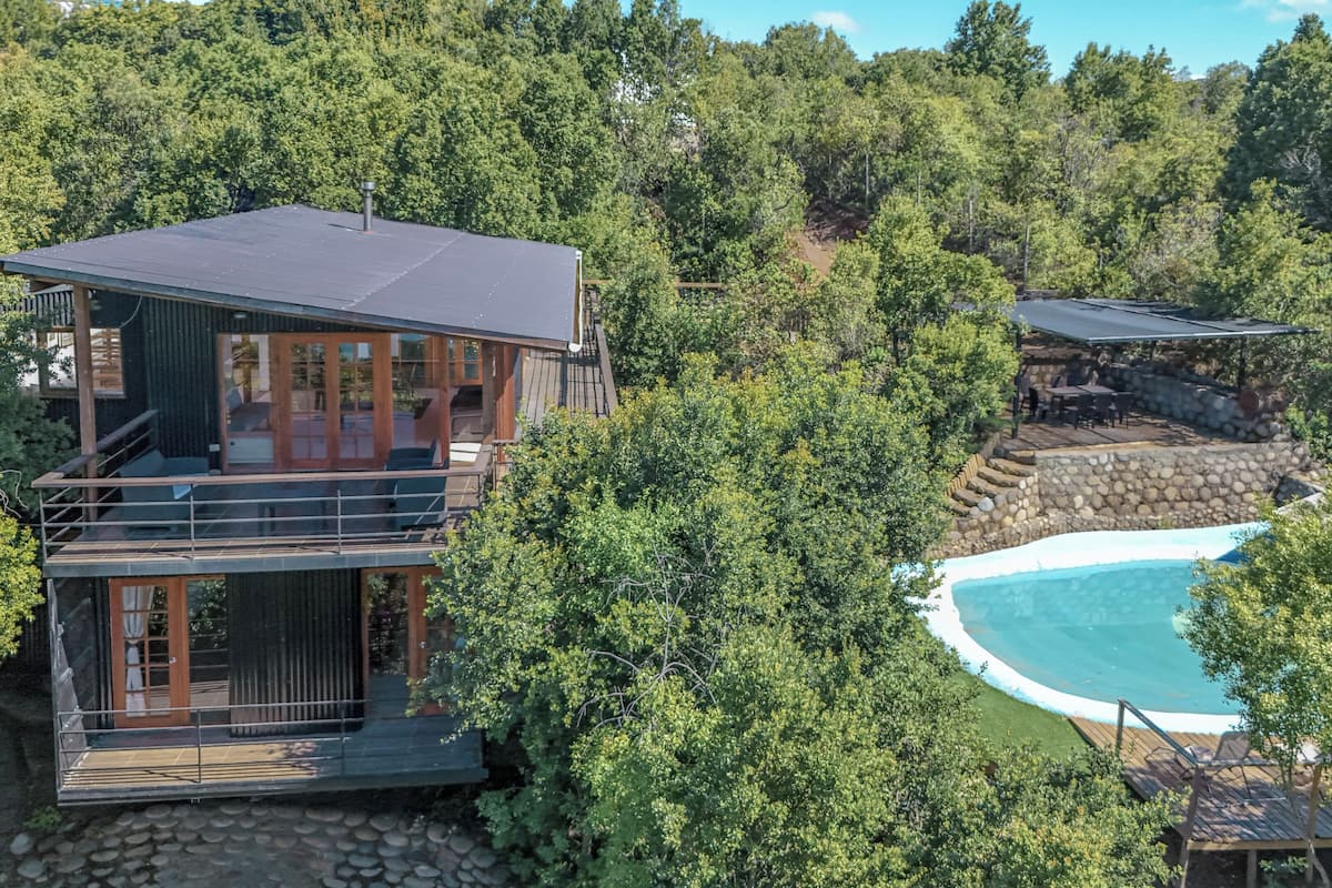 A modern two-story cabin with a pool surrounded by dense forest.