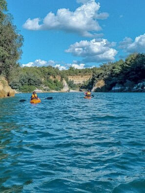 Dos kayakistas en un río tranquilo rodeado de acantilados y vegetación.
