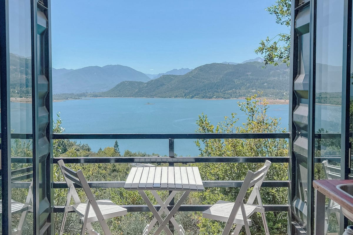 A balcony with a table and chairs, overlooking a lake and mountains.