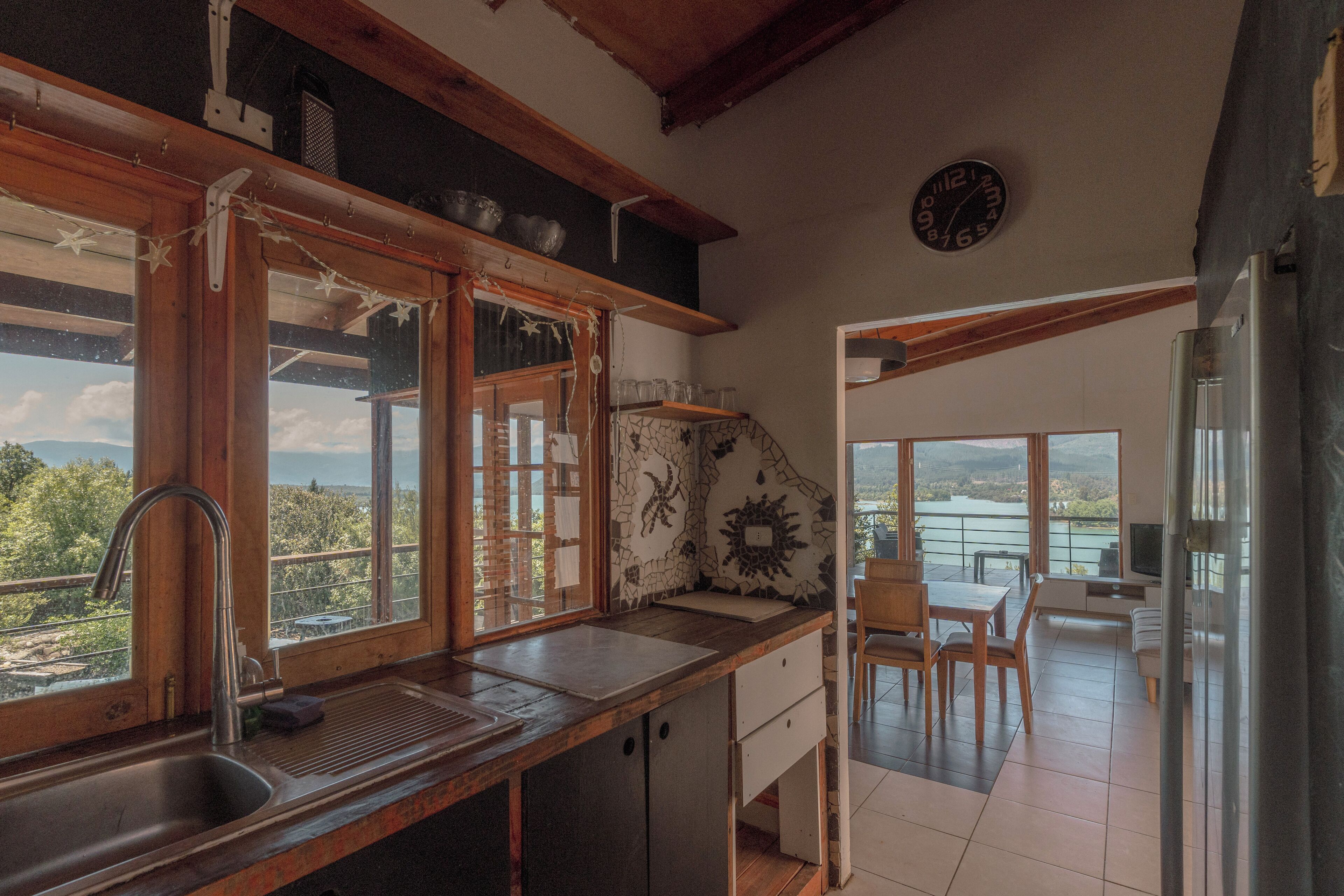 A kitchen with a wooden countertop, a sink, and a view of the outdoors. There is a dining area with a table and chairs.