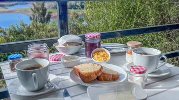 A breakfast table with bread, eggs, coffee, and condiments, overlooking a scenic landscape.