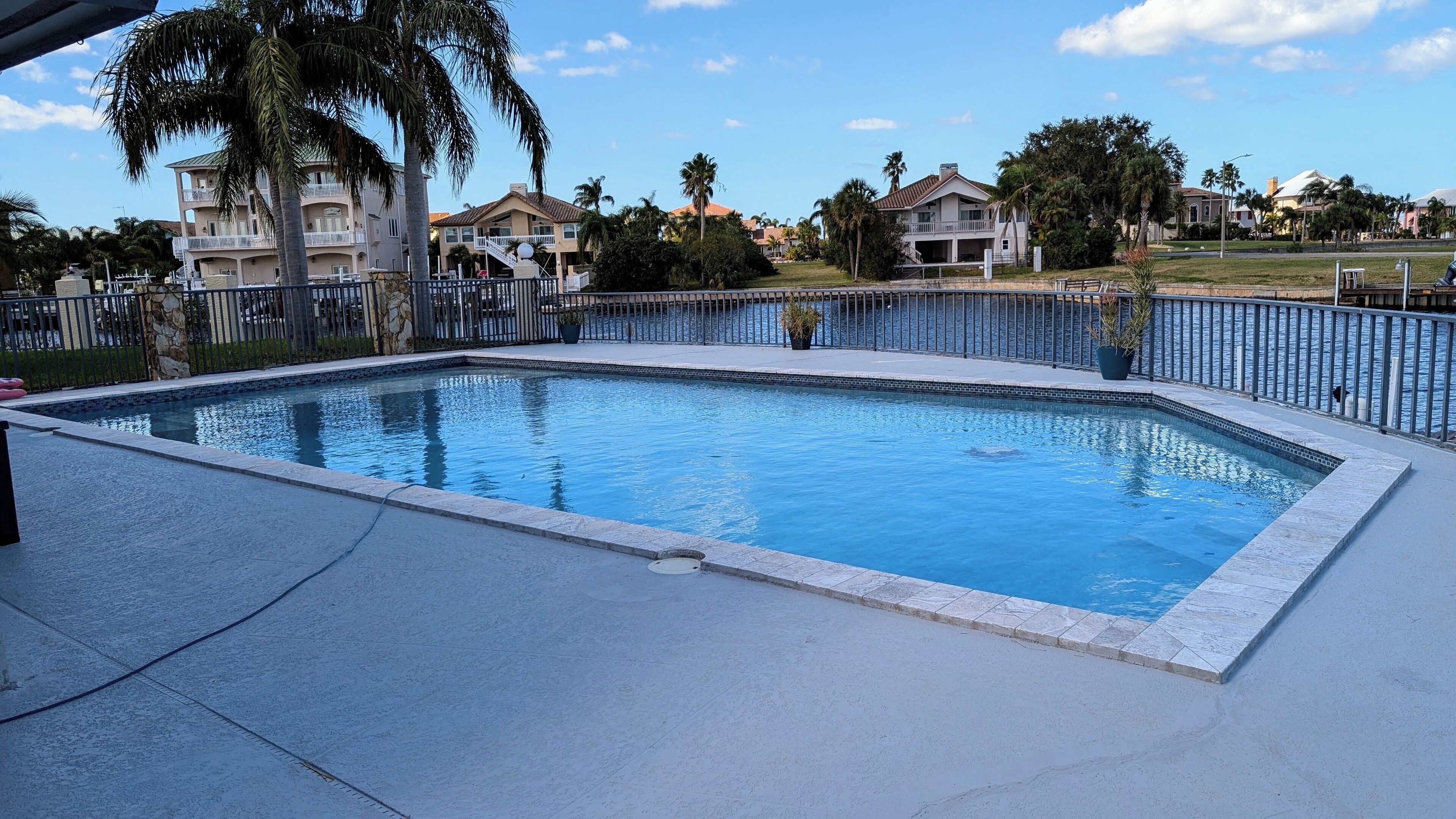 A rectangular swimming pool with a tiled edge, surrounded by a metal fence.