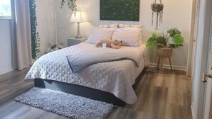A bedroom with a bed, ceiling fan, bedside lamps, a hanging plant, and a window with curtains.