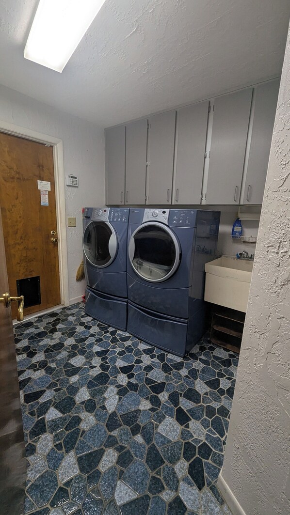 A laundry room with two front-loading washing machines, a sink, and cabinets above.