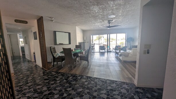 A spacious living area with a dining table and chairs, a sofa, and a large window providing a view of the outdoors.
