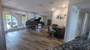 A spacious living area with a grand piano, a dining table, and a modern kitchen area.