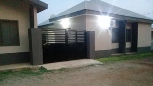 A modern building with a gated entrance, a concrete pathway leading to the door, and a grassy area in front. - MVH Apartment in Sunyani with free WiFi, AC and fully furnished kitchen. (Sunyani)