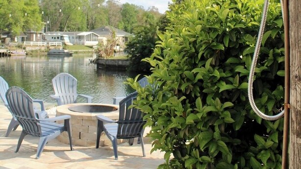 A patio with Adirondack chairs, a fire pit, and a view of a lake. - Entire Home Direct River Access Momma Marie’s (Spring Hill)