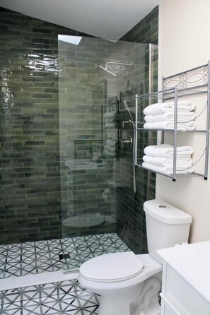 Une salle de bain moderne avec une douche à parois de verre, des toilettes blanches et un porte-serviettes où sont soigneusement pliées les serviettes.