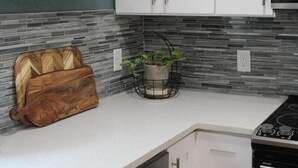 A kitchen with white cabinets, a stainless steel stove, a coffee maker on a shelf, and a potted plant. - Entire Home Direct River Access Momma Marie’s (Spring Hill)
