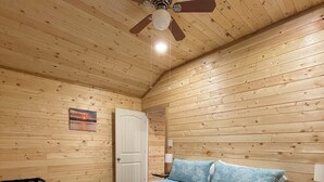 A bedroom with a wooden ceiling, a bed with a blue quilt, a ceiling fan, and a door.