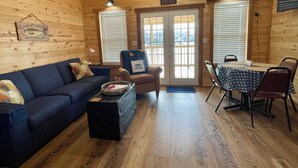 A cabin interior with a sofa, armchair, dining table, and a sign reading "Welcome to our cabin."