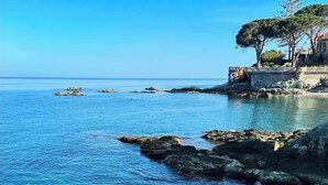 Paisaje costero con aguas azul turquesa, costa rocosa y un edificio rodeado de árboles.