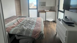 Una habitación compacta con una cama, un escritorio pequeño y un aparador.