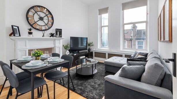 Un salon moderne avec une cheminée, une grande horloge, un téléviseur et un canapé gris.