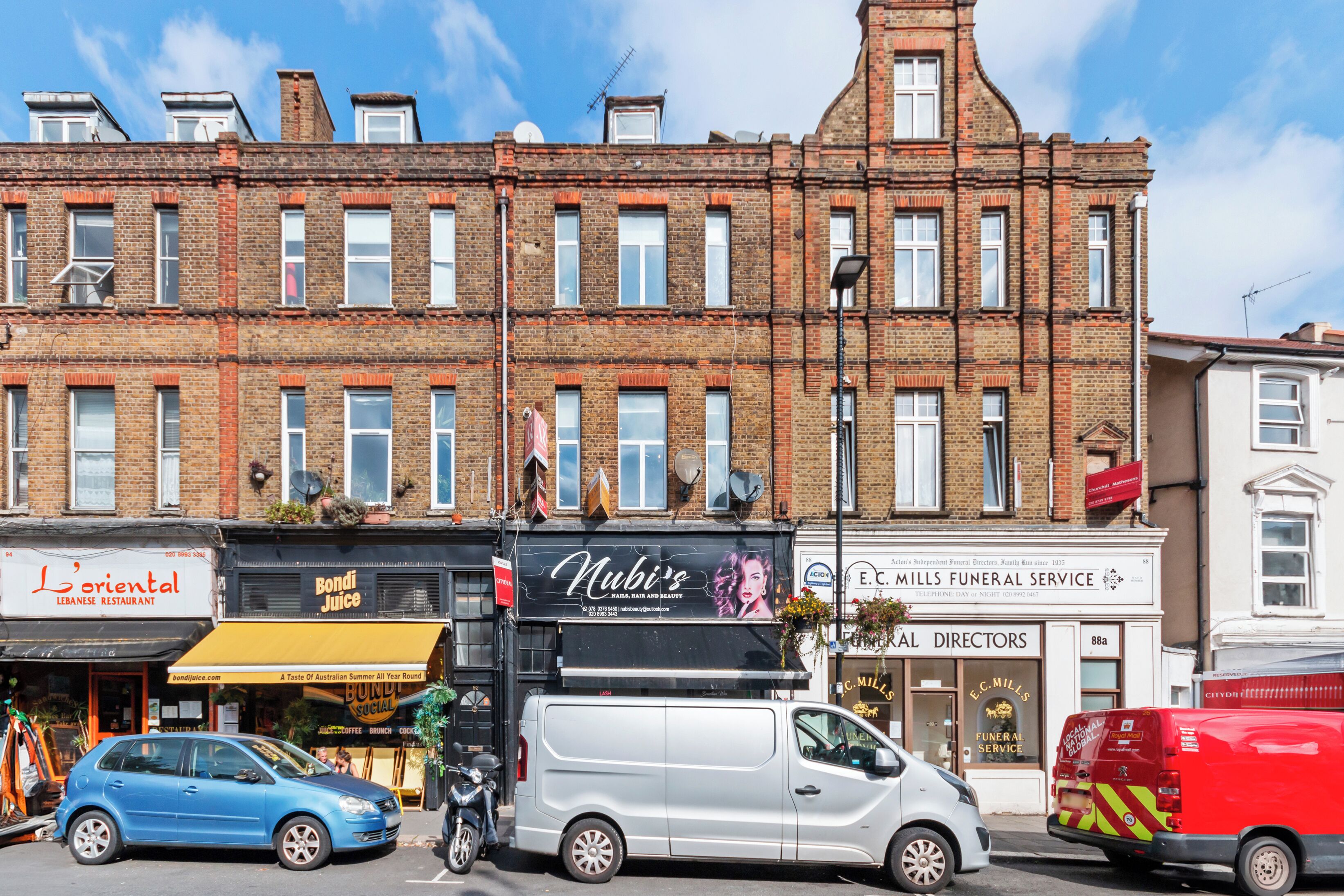 A multi-story brick building with various commercial establishments on the ground floor, including a restaurant, juice bar, and funeral service.