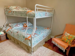 Un lit superposé avec une literie à motifs floraux, une petite table de chevet avec une lampe et une chaise avec un coussin.