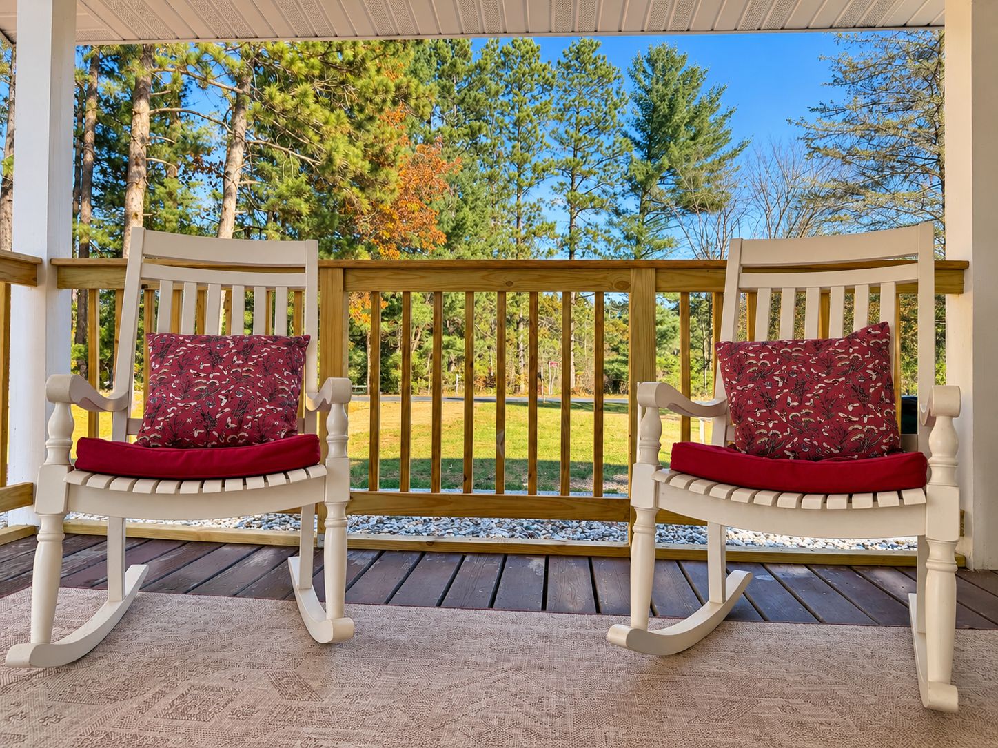 Two rocking chairs with red cushions on a wooden deck with a view of trees and grass.