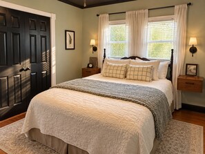 A bedroom with a large bed, two bedside tables, a nightstand, a door, and a window with curtains.