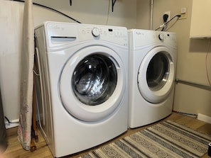 Une buanderie équipée de deux lave-linge Whirlpool Duet à chargement frontal, d’un tapis à motifs et d’un rideau.