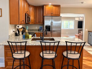 A kitchen with wooden cabinets, a stainless steel refrigerator, granite countertops, and three bar stools.