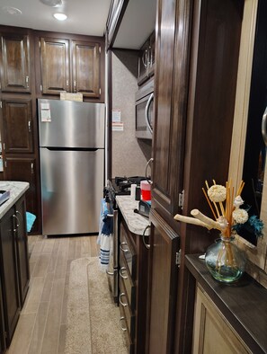 A modern kitchen with stainless steel appliances, wooden cabinets, and a marble countertop. - Cozy RV with all comforts of home in Horn town VA (Horntown)