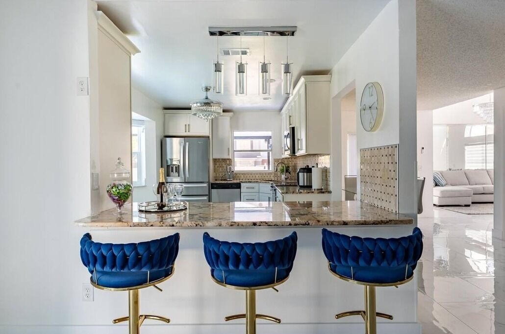 A modern kitchen with a central island, bar stools, and pendant lighting.