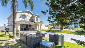 Ein zweistöckiges Haus mit überdachter Terrasse, Sitzgelegenheiten im Freien und einem Grill.