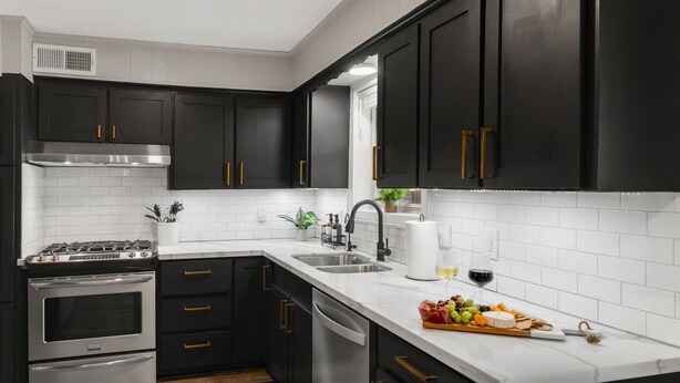 A modern kitchen with dark cabinets, stainless steel appliances, and a white countertop. - A&M Getaway • Game Room • Mini Golf • Sleeps 12 (Bryan)