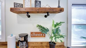 Une cuisine équipée d’une machine à café, d’une étagère en bois ornée de panneaux et d’une plante en pot.
