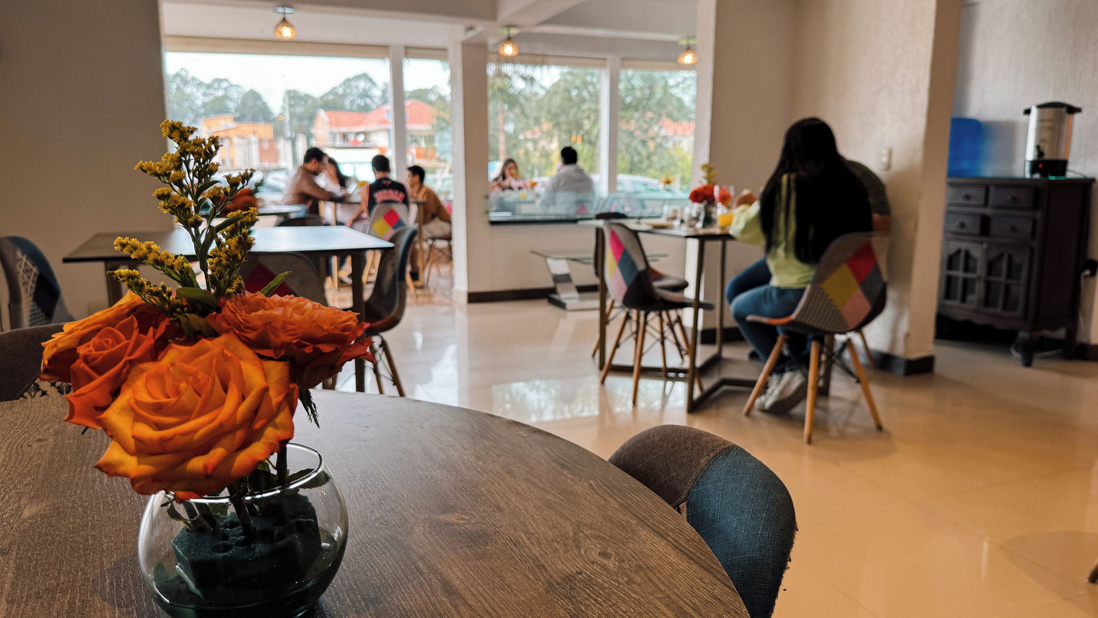 A dining area with a table featuring a vase of orange roses, a wooden table, and chairs.
