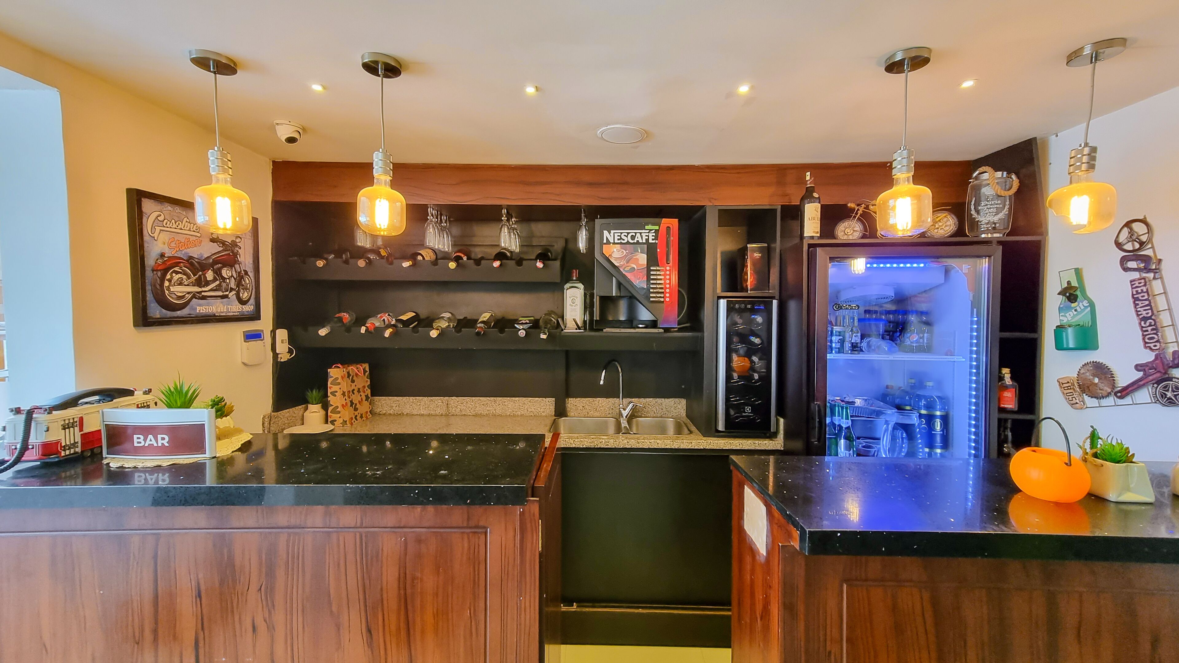 A modern kitchen with a bar area, featuring a refrigerator, wine bottles, and a coffee machine.