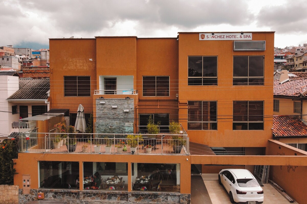 A hotel with a modern orange facade, large windows, and a visible car parking area.