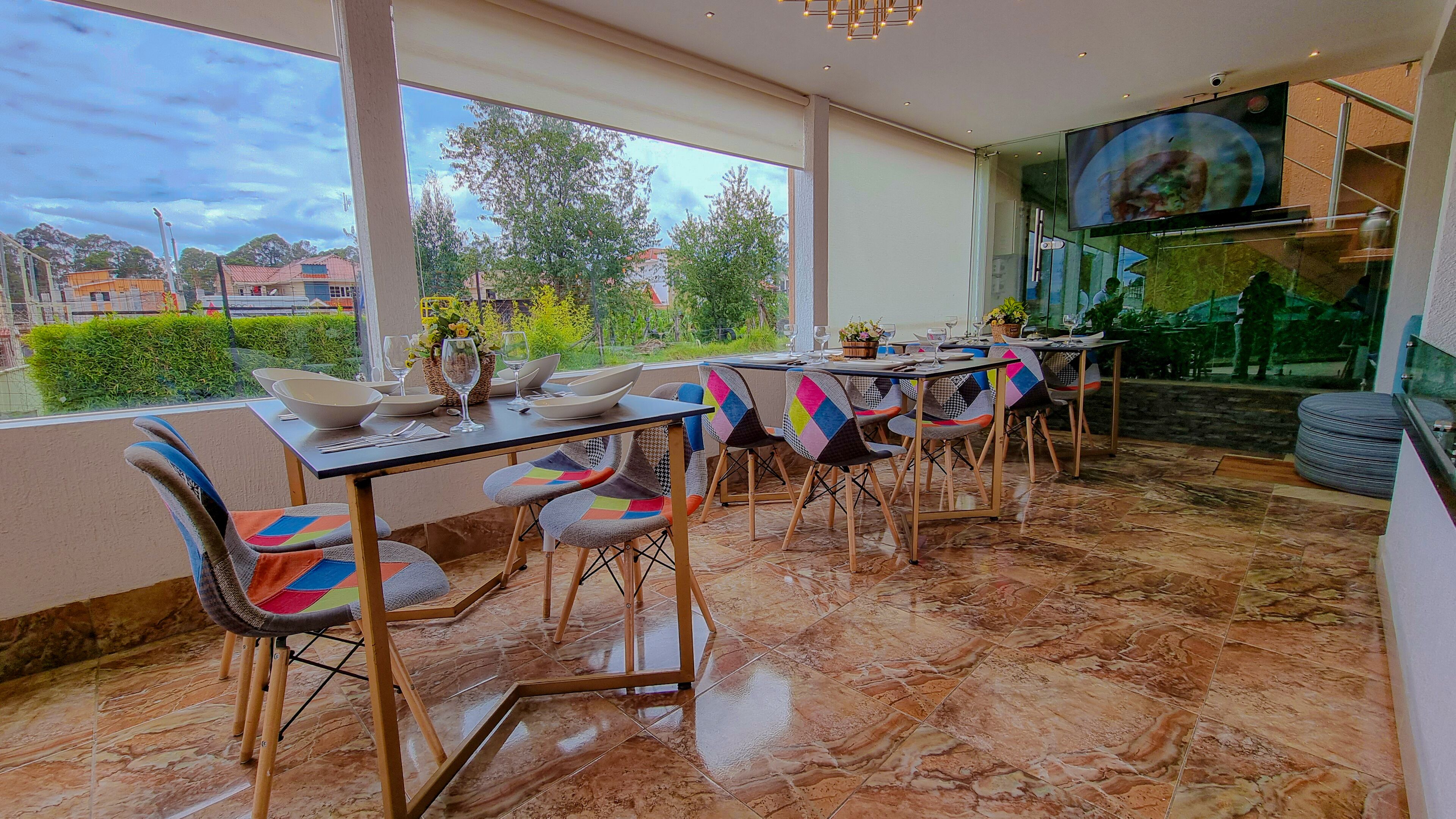 Un coin repas avec une table dressée pour quatre personnes, des chaises dotées de coussins colorés et une vue sur l’extérieur grâce à de grandes fenêtres.