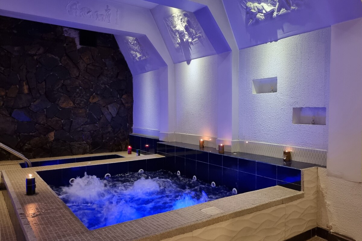 A spa area with a large hot tub, stone wall, and decorative lighting.