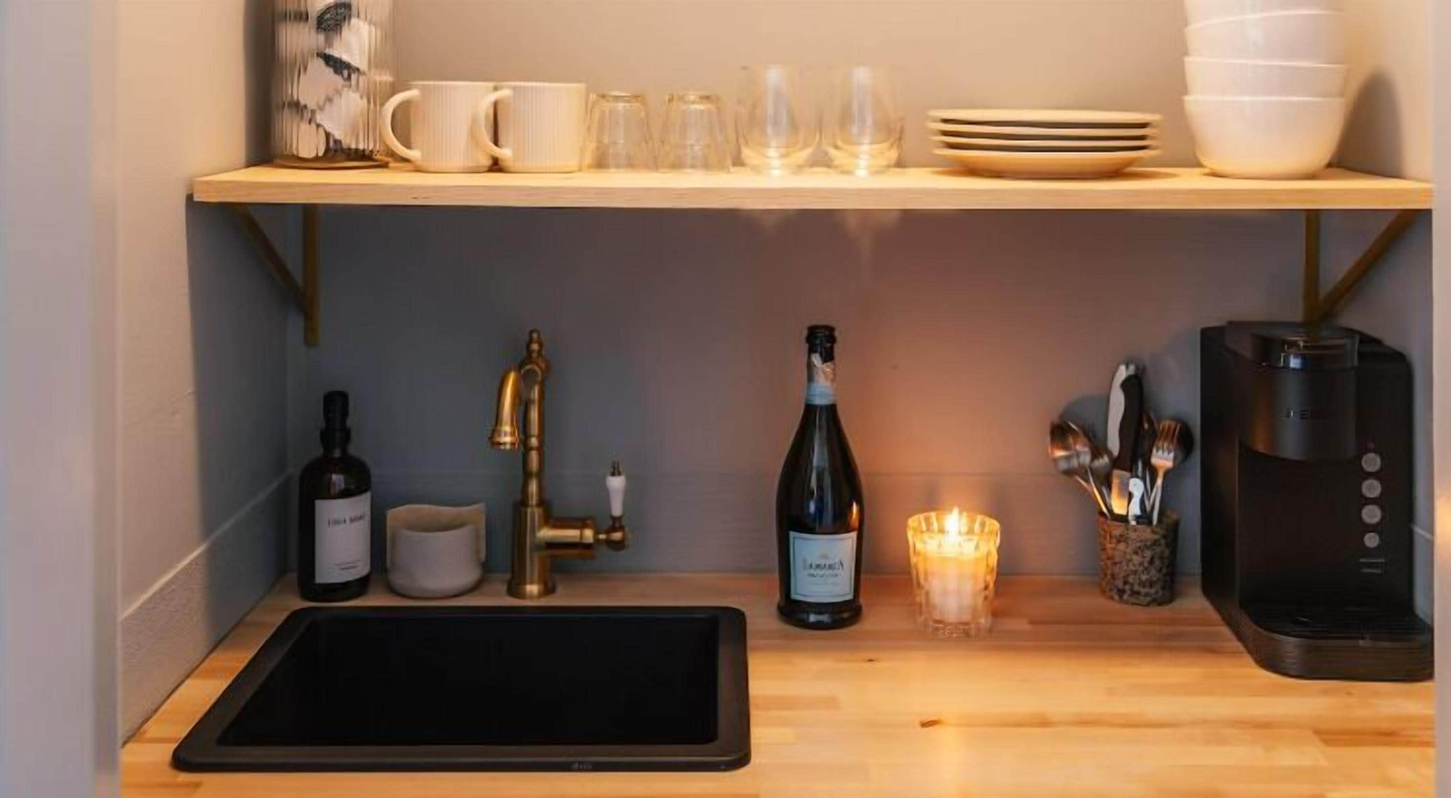 A kitchen with a wooden countertop, a sink, a coffee maker, a wine bottle, and a candle.