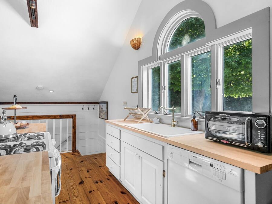 A modern kitchen with white cabinetry, a wooden countertop, a gas stove, a Bosch dishwasher, and a window with a view of greenery.