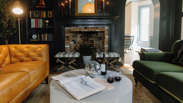 A cozy living room with a leather sofa, a round coffee table with books and a disco ball, a fireplace, and a bookshelf. - The Ipswich Inn (Ipswich)